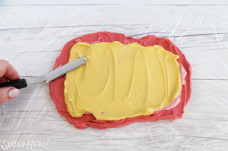 A small spatula spreading yellow buttercream on top of pink buttercream.