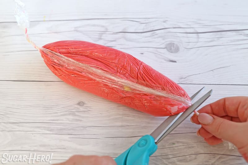 Snipping the end of a plastic wrap-covered buttercream tube.