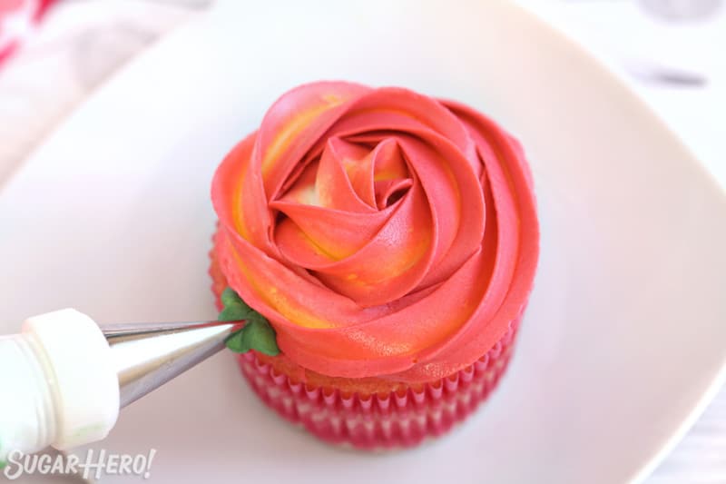 Piping green buttercream leaves to the side of a Rosette Cupcake.