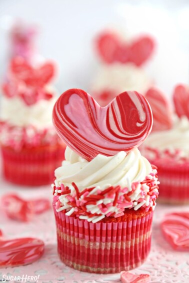 Close-up of cupcake with white buttercream, pink and red sprinkles, and a large chocolate heart on top.