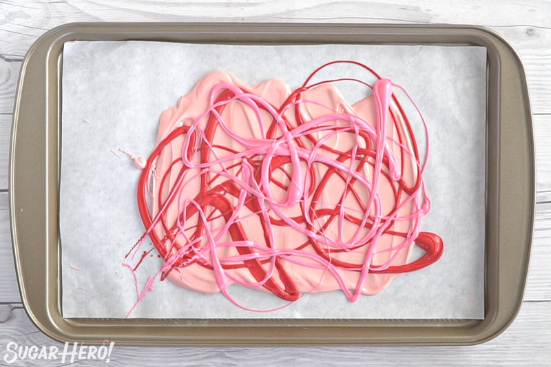 Drizzling red and pink candy melts on top of each other on a parchment-covered baking sheet.