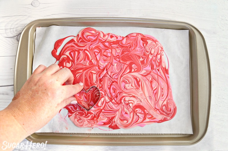 Hand cutting heart shapes out of pink and red swirled candy melt bark.
