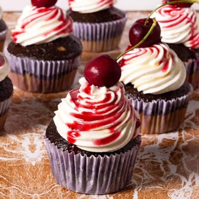 Chocolate Cherry Cupcakes with big swirls of white frosting, cherry sauce, and fresh cherries on top.