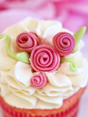 Close-up of a cupcake with white buttercream and pink fondant roses on top.
