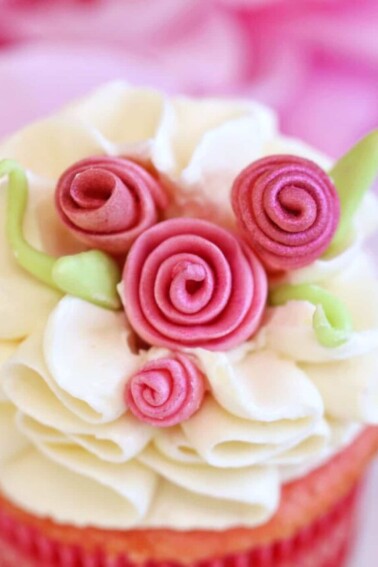 Close-up of a cupcake with white buttercream and pink fondant roses on top.