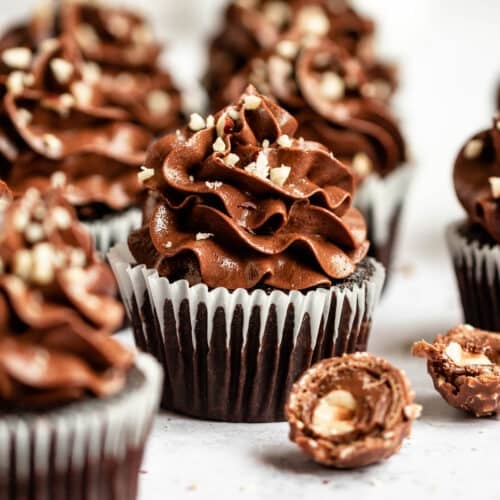 Close up of a few few Nutella Cupcakes on a white surface next to hazelnuts.