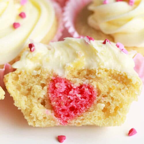 Close-up of a vanilla cupcake with a pink cake heart embedded in the center.