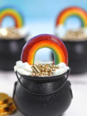 Three Pot of Gold Cake Cups on a white marble surface with gold coins scattered around.