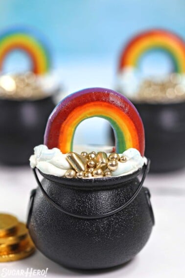 Three Pot of Gold Cake Cups on a white marble surface with gold coins scattered around.