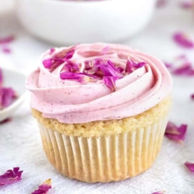 Vanilla cupcake with swirled pink frosting and purple rose petals on top.