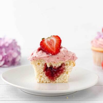 Single Strawberry Filled Cupcake on a white plate cut in half to show interior.