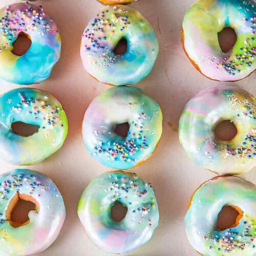 Overhead shot of rainbow doughnuts with swirled pastel frosting and sprinkles.