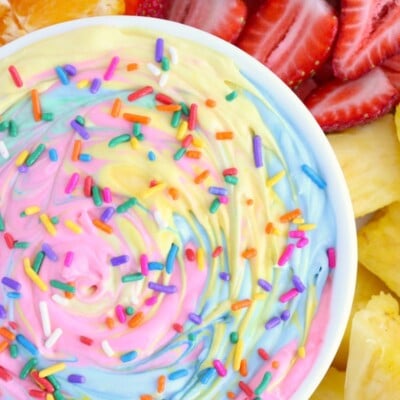 Overhead shot of a bowl of swirled rainbow dessert dip surrounded by fruit.