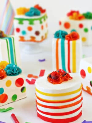 Group of multi-colored Birthday Present Mini Cakes on white background with confetti and candles scattered around.
