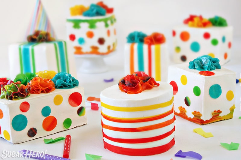 Group of multi-colored Birthday Present Mini Cakes on white background with confetti and candles scattered around.