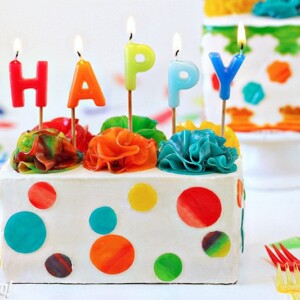 White rectangular cake with candy polka dots and lit birthday candles on top.