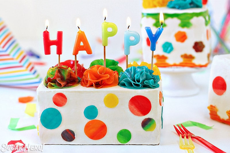 White rectangular cake with candy polka dots and lit birthday candles on top.