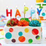 White rectangular cake with candy polka dots and lit birthday candles on top.