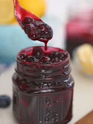 A glass jar full of blueberry sauce with a spoonful dripping over the top of the jar.