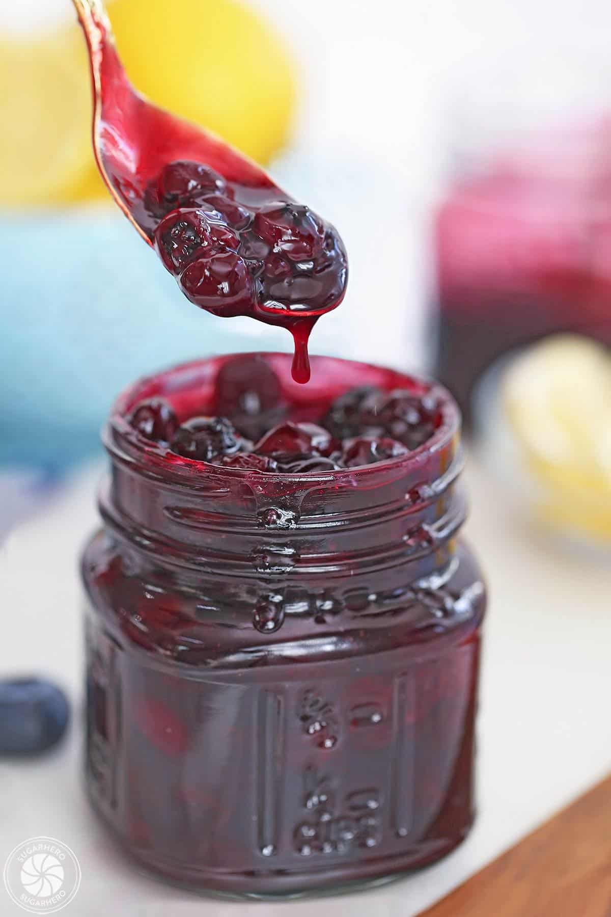 A glass jar full of blueberry sauce with a spoonful dripping over the top of the jar.