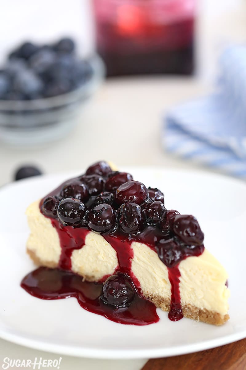 A piece of cheesecake covered with blueberry sauce on a round white plate.