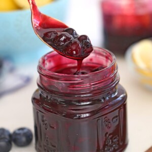 Close up of blueberry sauce in a glass mason jar with a spoonful of blueberry sauce hovering over the jar.