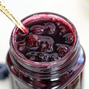 Close up of blueberry sauce in a glass mason jar with a gold spoon in it.