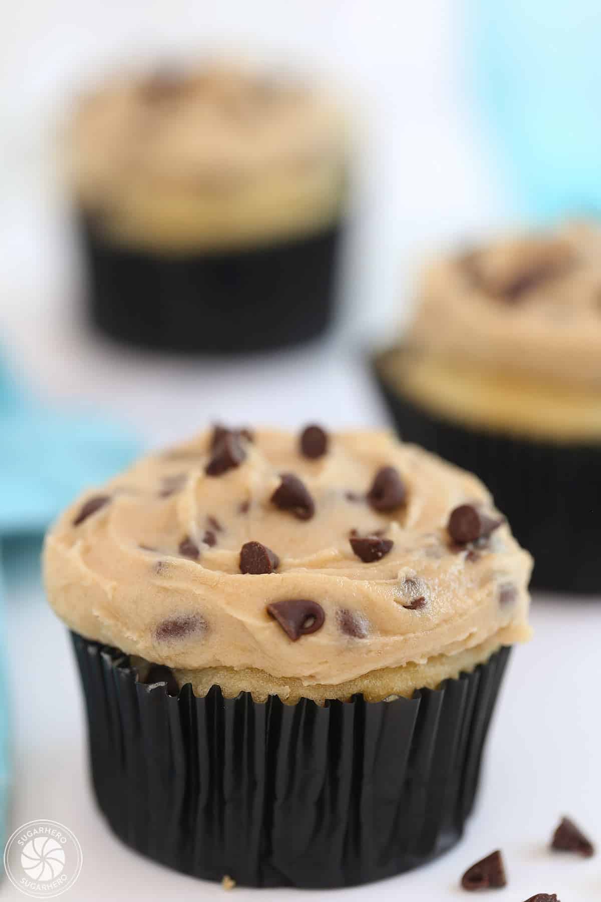 Three cupcakes frosted with Cookie Dough Frosting on a white surface with a blue napkin behind them.