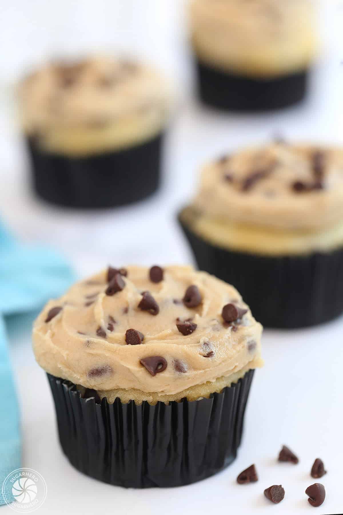 Four cupcakes frosted with Cookie Dough Frosting on a white surface with a blue napkin behind.