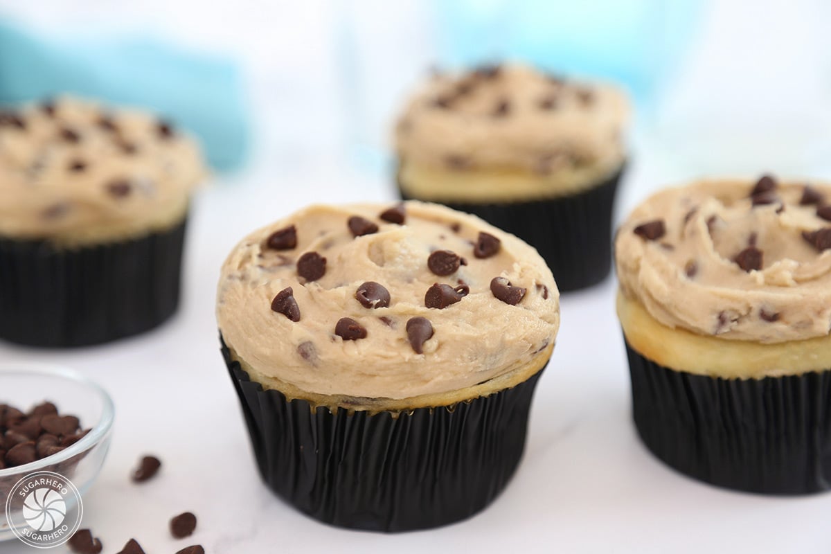 Four cupcakes frosted with Cookie Dough Frosting on a white surface with a blue linen behind them.