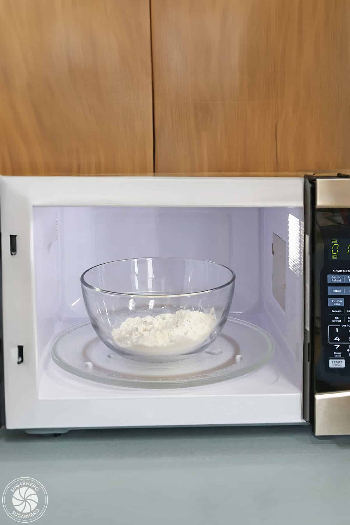 Flour in a glass bowl set in a microwave with the time set for 1 minute.