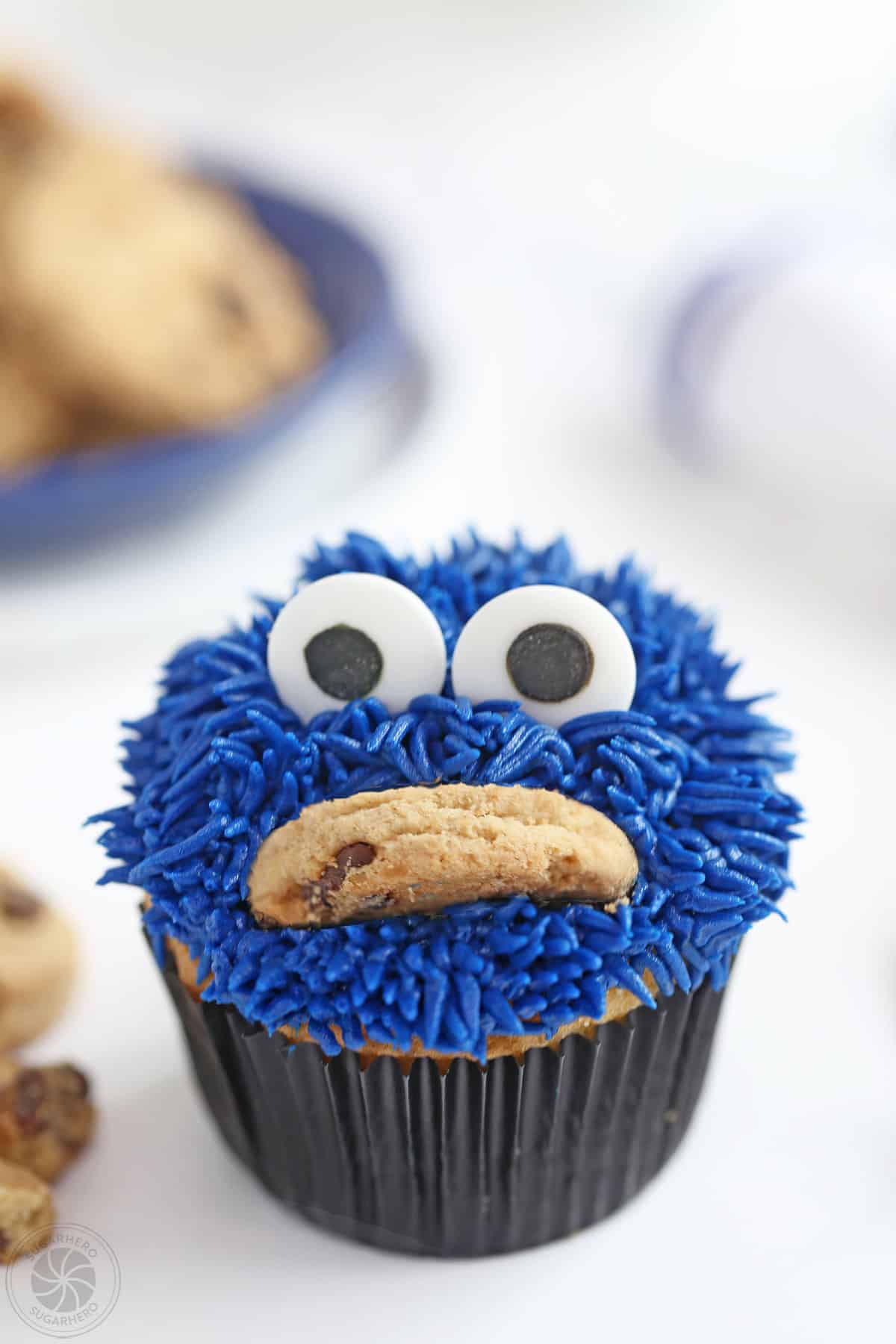 Close-up of a Cookie Monster Cupcake with a blue plate of cookies in the background.