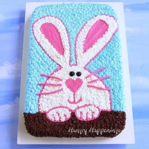 Sheet cake decorated with a pink and white Easter bunny on a white cake board.