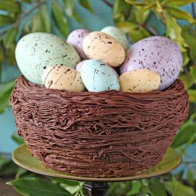 Close up of Easter Nest Cake on a green cake stand surrounded by greenery.