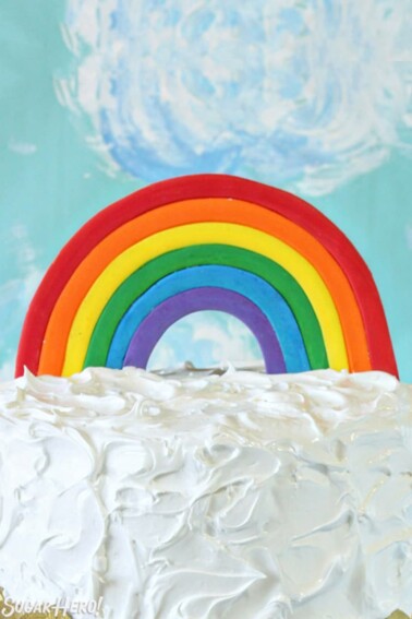 Fondant Rainbow Cake Topper on top of a cake frosted with fluffy white frosting.