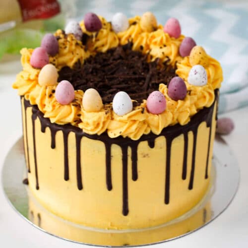 Yellow layer cake with chocolate drip, buttercream swirls, and mini eggs on top.
