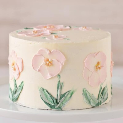 White layer cake with buttercream flowers painted on the sides.