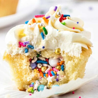 Vanilla cupcake with a bite taken out of it, showing sprinkles and candies hidden inside.