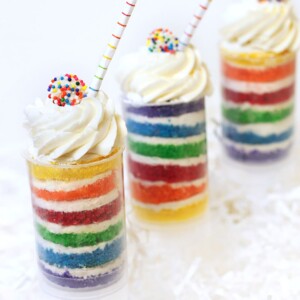 Three Rainbow Cake Push-Up Pops in front of a white background with striped straws sticking out.