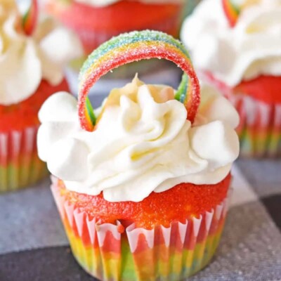 Close-up of rainbow cupcake with frosting and a rainbow candy strip on top.