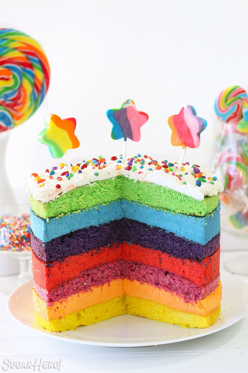 Rainbow Mousse Cake with several slices cut out of it, with star-shaped lollipops on top.