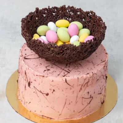 Pink layer cake with chocolate speckles and a chocolate nest on top filled with Easter candy.