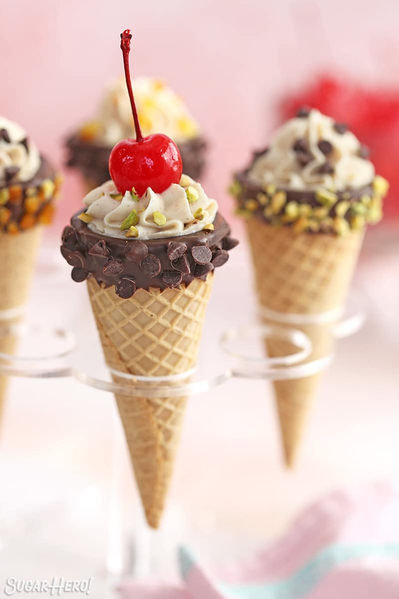 Cannoli cones in an ice cream holder, decorated with nuts, chocolate chips, and cherries.