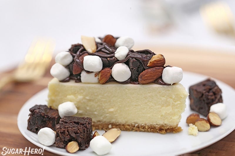 Slice of cheesecake with brownie chunks, marshmallows, and almonds on top.