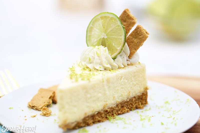 Slice of cheesecake with lime zest, lime slices, and graham crackers on top.