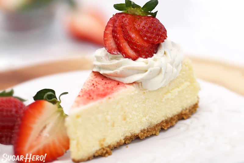 Slice of cheesecake with strawberry dust and fresh strawberries on top.