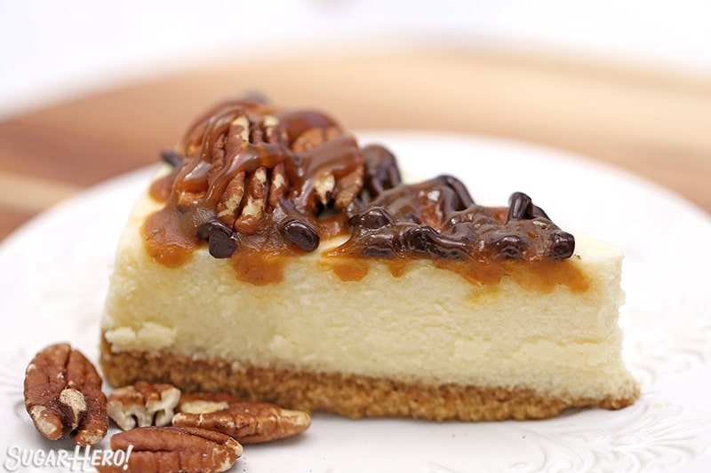 Slice of cheesecake with chocolate sauce, caramel sauce, and toasted pecans on top.