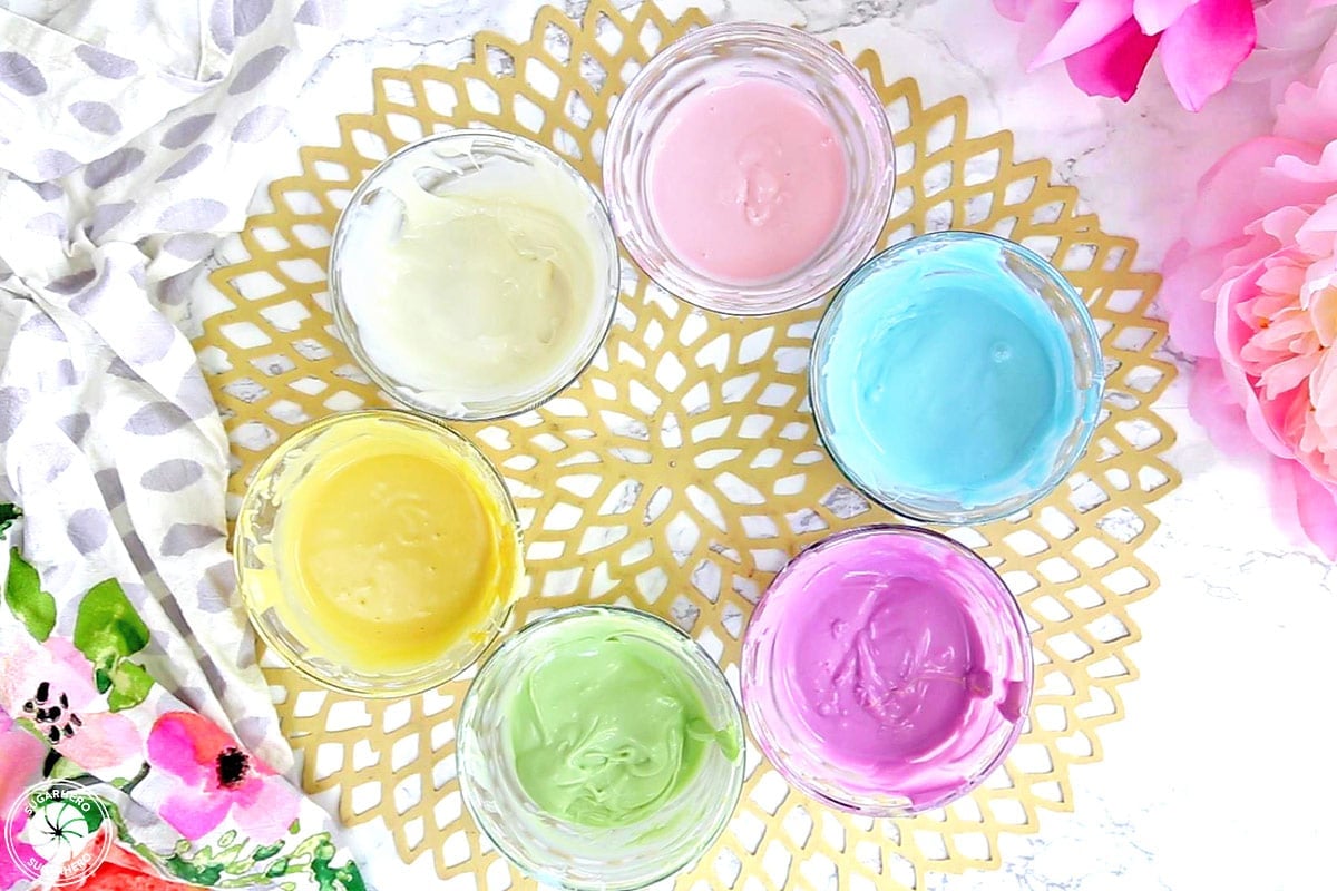 Overhead shot of six different colors of melted candy coating in small glass bowls.