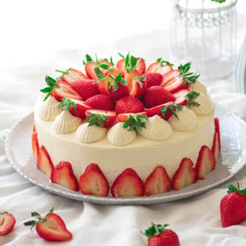 Japanese shortcake on white platter with fresh sliced strawberries on top and around the sides.