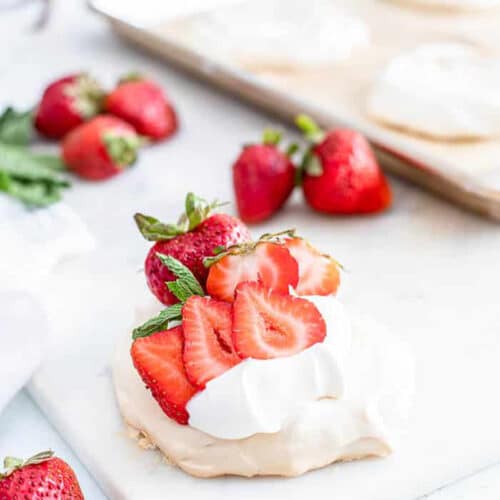 A strawberry mini pavlova on a white cutting board with fresh strawberries and a wooden board in the background.